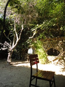 Chair on dirt beneath trees; stone wall with low arch beyond