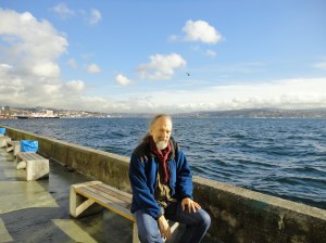 Myself on a bench, with scarf and fleece jacket, the Bosphorus behind me, clouds above
