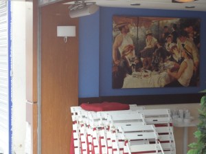 Reproduction of “Boating Party” on wall of an alcove; folded chairs below