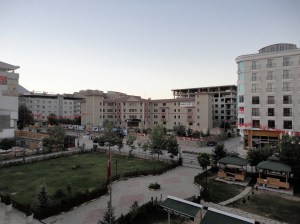 A plot of grass with boxy buildings around it; the sun has not yet reached them