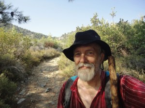 Selfie with black hat and hiking staff on trail through bushes