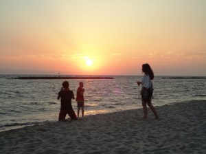 Three figures on the beach enjoy the setting sun