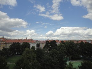 Trees and roofs form low horizon against blue sky with clouds