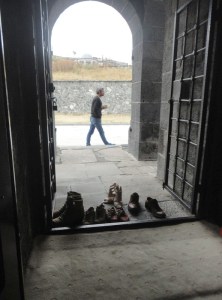 Five pairs of shoes stand just outside the threshold. Beyond is an archway, and just outside that is a man walking past