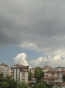 Gray clouds over blue sky over white clouds over buildings