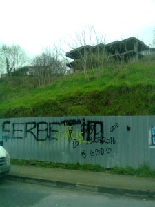 Building skeleton atop grassy hill, fenced off at base