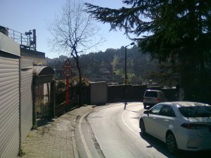 Road scene: Two lanes, narrow sidewalk, then garage doors and walls; but beyond, a green hillside