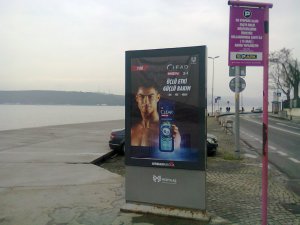 On a billboard by the sea, a young man with bare shoulders thrusts at us a dark blue bottle of shampoo and shower gel. The background of the advertisement is black.