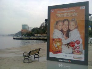 On another billboard by the sea, a smiling woman is cheek to cheek with each of two smiling little girls. All are wearing white tops, and the background is orange, for a product in an orange box: fish oil