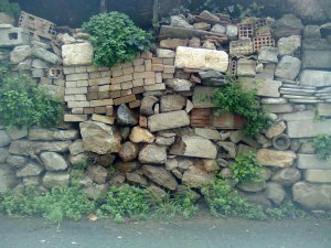 Wall assembled haphazardly of rubble, dressed stone, brick, and tile; weeds grow out here and there
