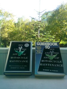 Two books: Zen and the Art, and the Guidebook to it, the latter featuring an image of the former on its cover; the top of a pine tree beyond, and beyond that, more trees and an apartment building