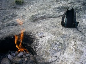 Flame the size of a nearby backpack jets from a blackened rock