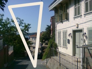 Isosceles triangle superimposed over a view down a steep street, clapboard house on the right, garden wall and trees on the left, sea in the distance