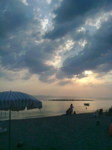 Clouds in front of setting sun on a beach with an umbrella and a family on the shore