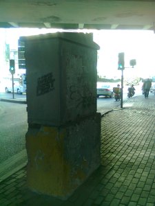 Beyond the dark box and the shade of the elevated highway, cars, motorcycles, and pedestrians enter the sunlight