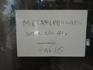 Handwritten sign in shop window: ΜΕΤΑΦΕΡΘΗΚΑΜΕ …