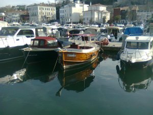 Boats docked in a marina; beyond them, white boxy buildings
