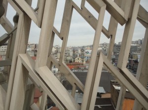The façade of a church with two towers appears among other buildings through a decorative concrete lattice of lozenges
