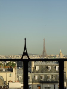 Photo: Appearing the same size are the Eiffel Tower in the distance and a model in the foreground, standing on the railing of a window that overlooks other buildings