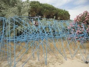Lying on edge against a backdrop of pine trees and oleander, steel rods trace out the edges of shallow pyramids on square bases, with perpendiculars dropped from the apices to the edges of those bases