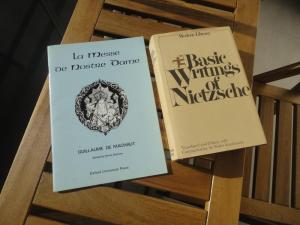 La Messe de Nostre Dame (saddle-bound paperback) and The Basic Writings of Nietzsche (perfect-bound hardback) on slatted wooden table next to slatted wooden chair